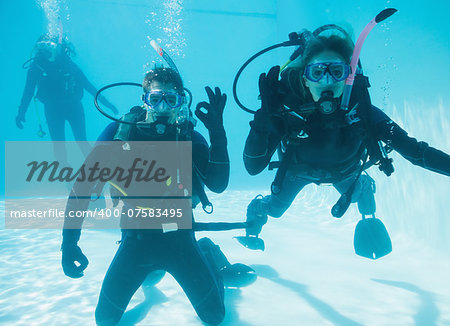 Friends on scuba training submerged in swimming pool two looking to camera on their holidays