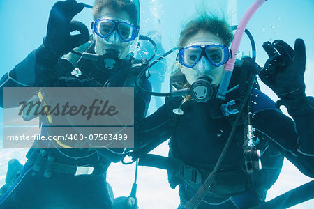 Friends on scuba training submerged in swimming pool looking to camera on their holidays
