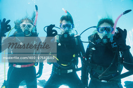 Friends on scuba training submerged in swimming pool looking to camera  on their holidays