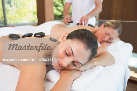 Calm friends lying on massage tables with hot stones on their backs in the health spa