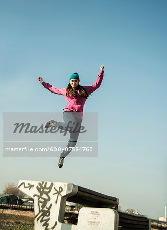 Teenage girl jumping over bench outdoors, industrial area, Mannheim, Germany