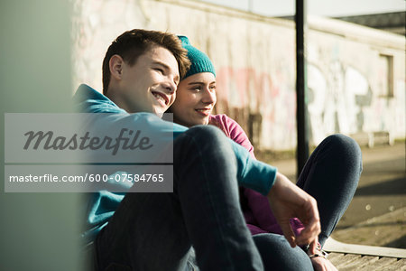 Teenage girl and boy sitting on ground, smiling and looking at view together, Mannheim, Germany