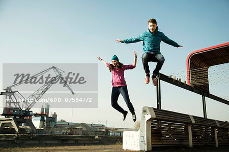 Teenage girl and boy jumping over bench outdoors, industrial area, Mannheim, Germany Teenage girl and boy jumping over bench outdoors, industrial area, Mannheim, Germany