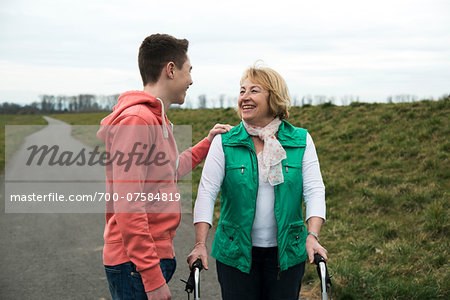 Teenage grandson talking to grandmother using walker on pathway in park, walking in nature, Germany Teenage grandson talking to grandmother using walker on pathway in park, walking in nature, Germany