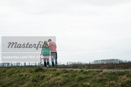 Backview of teenage grandson with grandmother using walker on pathway in park, walking in nature, Germany