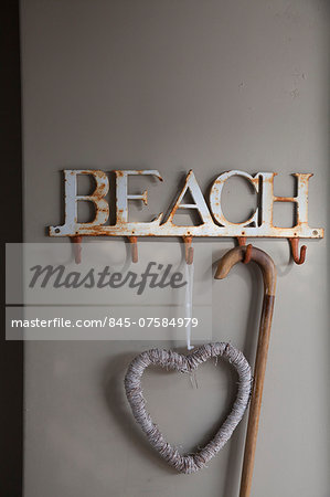Rusty beach named hat rack with white straw heart decoration and wooden walking stick in South African beach house