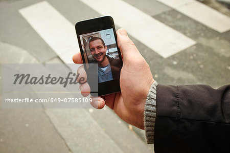 Mid adult man on sidewalk holding smartphone with photograph on screen