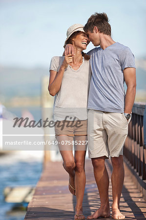 Young couple walking along jetty, arms around each other