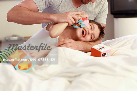 Father and young son playing with building blocks on bed