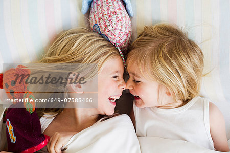 Portrait of two young sisters lying face to face in bed