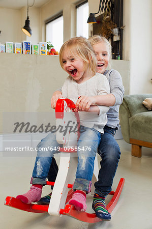 Two young sisters playing on rocking horse Two young sisters playing on rocking horse