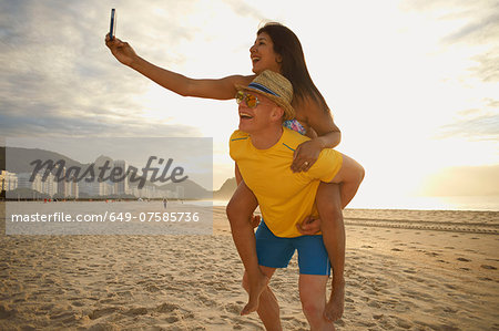 Couple taking self portrait on smartphone, Copacabana beach, Rio De Janeiro, Brazil