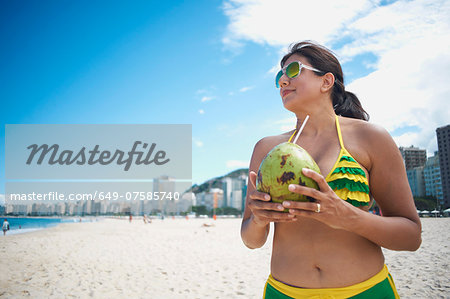 Mature woman drinking from coconut on Copacabana beach, Rio De Janeiro, Brazil