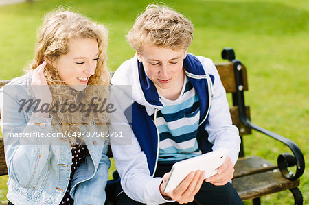 Teenage siblings looking at digital tablet on bench