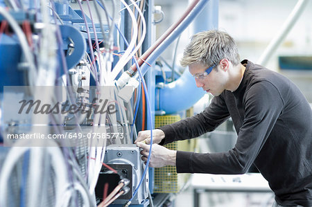 Mid adult male technician maintaining cables in engineering plant