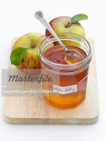 A glass jar of apple jelly with whole apples behind
