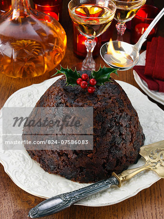 Whole Xmas pudding with brandy decanter and glasses in the background ladle of flaming brandy