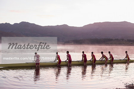Rowing crew placing scull in lake at dawn