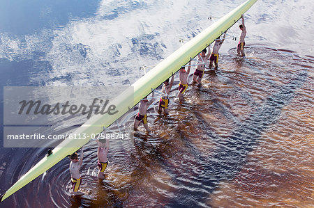 Rowing crew carrying scull overhead in lake