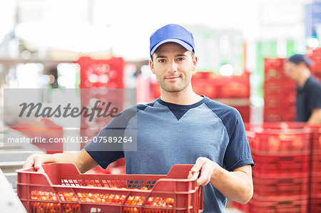 Portrait of confident worker holding crate of tomatoes in food processing plant