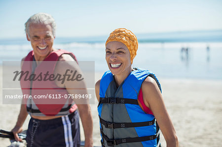 Enthusiastic couple in life jackets on beach