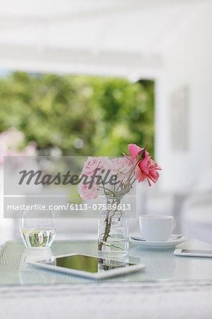 Pink roses on patio table next to coffee cup and digital tablet Pink roses on patio table next to coffee cup and digital tablet