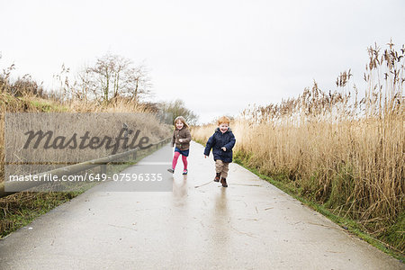 Young sister and brother running along rural road