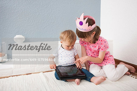 Girl watching over baby boy playing digital tablet