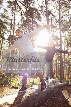 Twin brothers walking along fallen tree trunk in forest