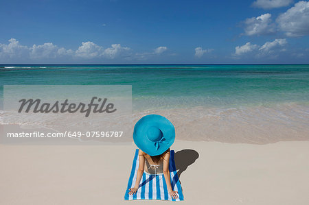 Young woman relaxing on beach with blue sunhat