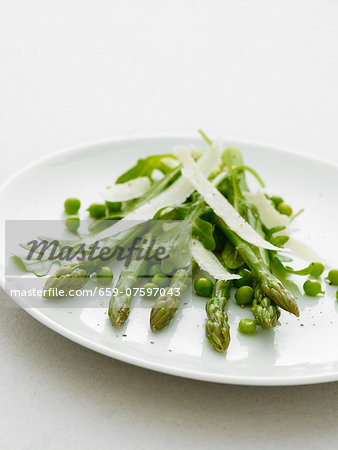 Asparagas and peas with parmesan shavings on a white plate