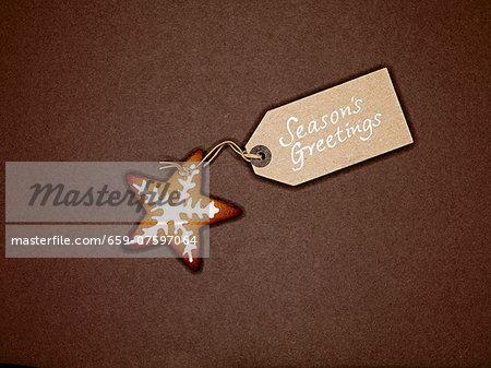 Star shaped ginger bread biscuit with white icing, and Christmas gift-tag, on a brown background