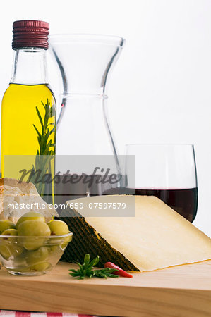 A still life featuring olive oil, red wine, bread, olives and Manchego (Spain)