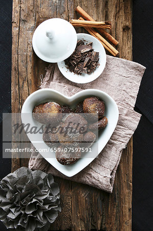 Chocolate and cinnamon treats in a heart-shaped bowl, grated chocolate, cinnamon sticks