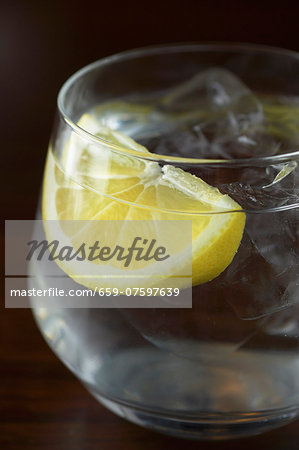 A glass of water with a wedge of lemon and ice cubes