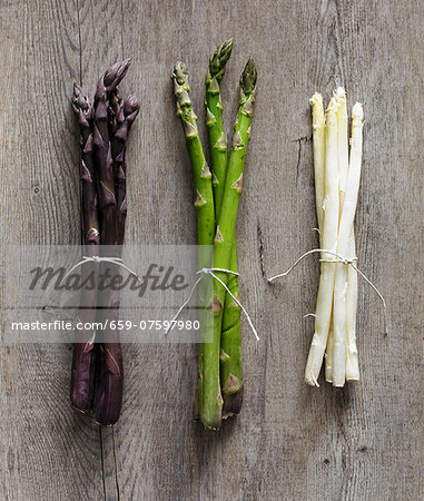 Purple, green and white asparagus stalks on a wooden surface