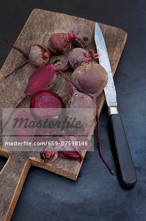 Several boiled beetroot, some peeled, on a wooden board with a knife