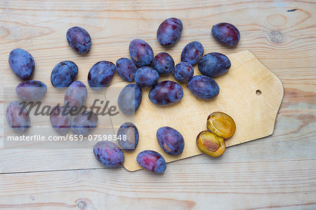 Fresh plums on a chopping board and on a wooden surface