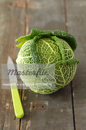 A young savoy cabbage on a wooden surface with a knife