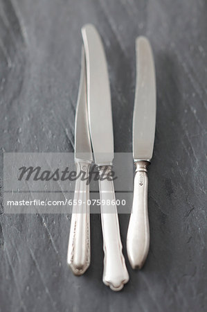 Three knives on a slate surface