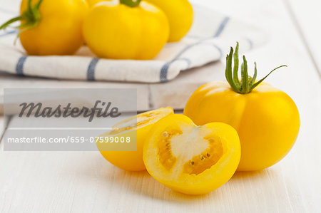 Yellow tomatoes (of the variety Golden Queen), whole and cut in half, on a white kitchen table