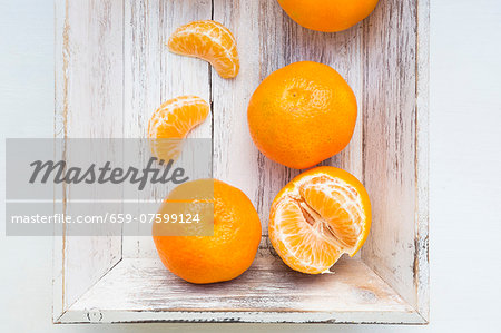 Clementine oranges, whole and peeled, on a wooden tray