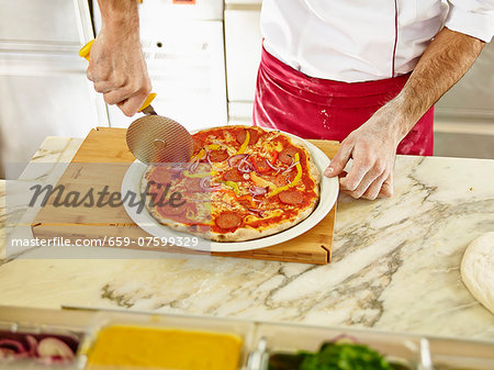 A chef cutting a pizza into portions using a pizza wheel