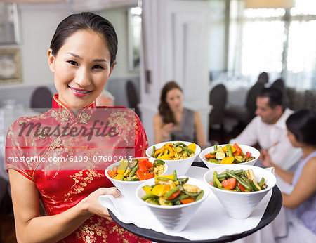 Waitress carrying food tray with people at dining table in restaurant