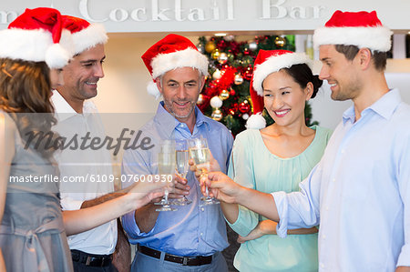 People in Santas hats toasting champagne flutes at bar