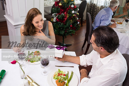 Man giving gift box to smiling woman in restaurant