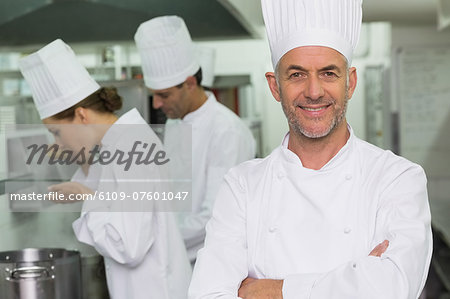 Happy chef looking at camera with team working behind