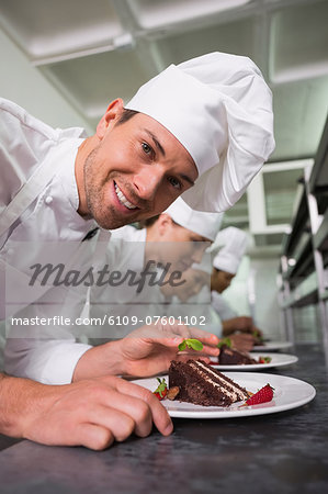 Row of chefs garnishing dessert with one smiling at camera