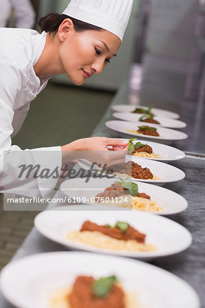Happy chef putting basil leaf on spaghetti dish