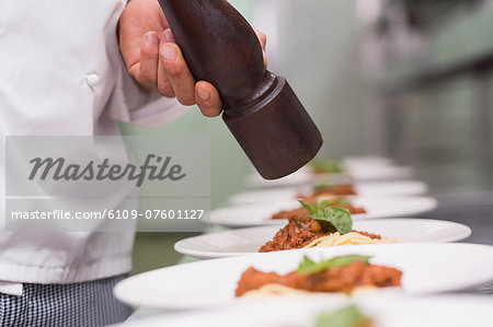 Chef grinding pepper over spaghetti dish